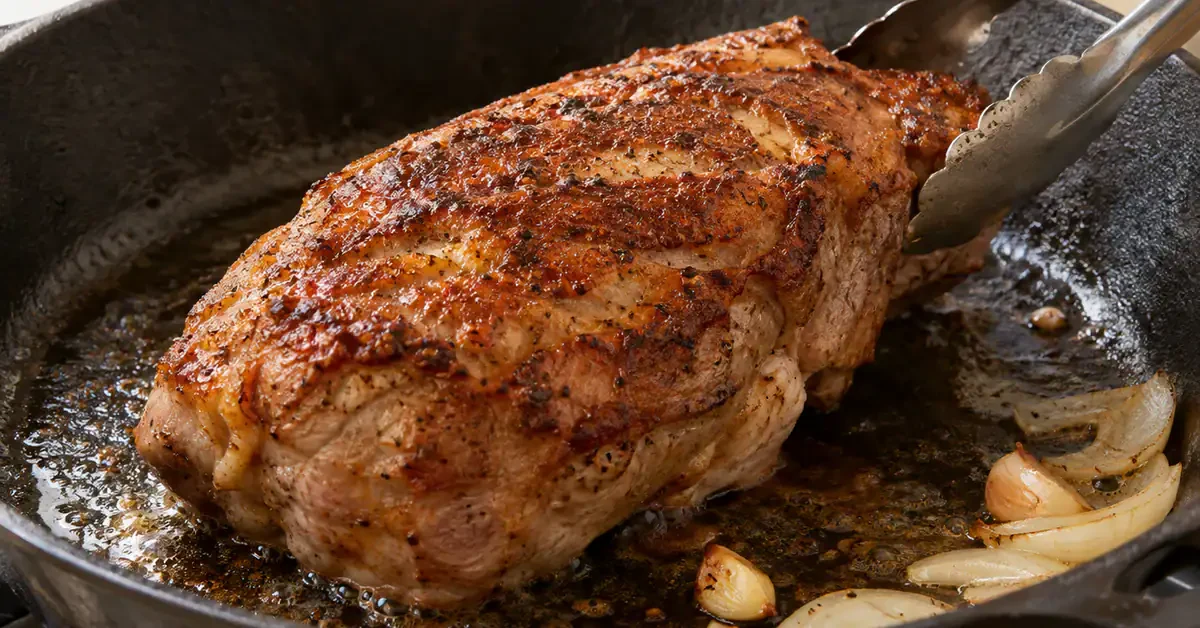 Pork browning beside onion in a pan Pork browning beside onion in a pan